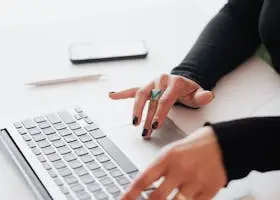 A businesswoman's hands typing on a laptop at a bright, modern workspace.